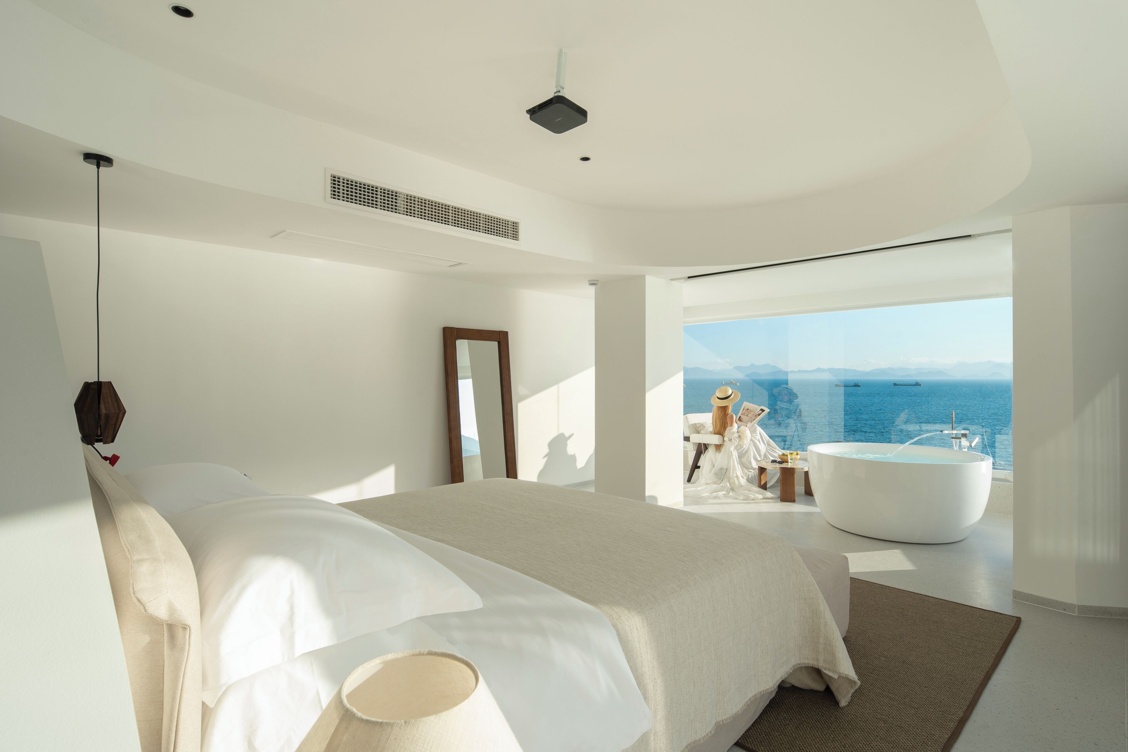 Ein modernes Schlafzimmer mit einem großen Bett, Meerblick und einer Badewanne.