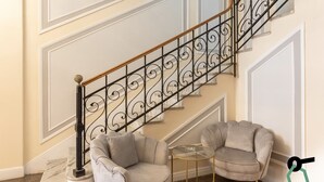 Un escalier orné de rampes noires et un sol en marbre. On y trouve deux fauteuils gris et une petite table ronde avec un plateau en verre.
