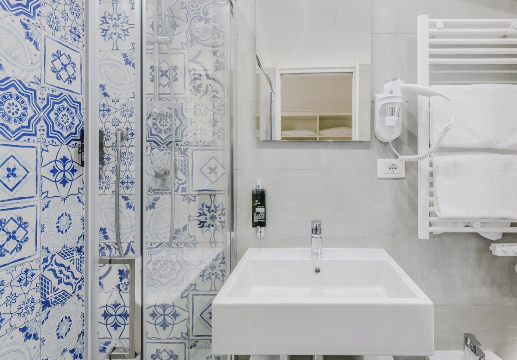 A bathroom with a white sink, a towel rack, and a shower with blue and white patterned tiles.