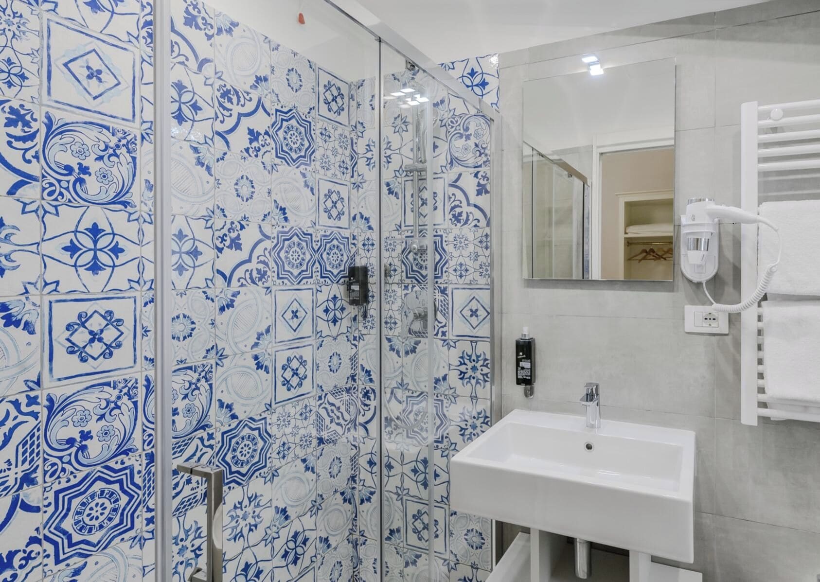 Een badkamer met een wit wastafelmeubel, een spiegel en een douche met blauw betegelde wanden.