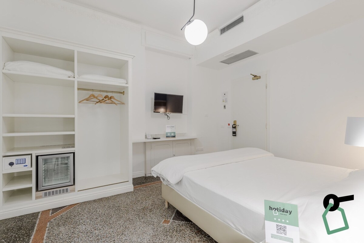 A hotel room with a bed, a wardrobe, a television, a heater, and a sign indicating a holiday rate.