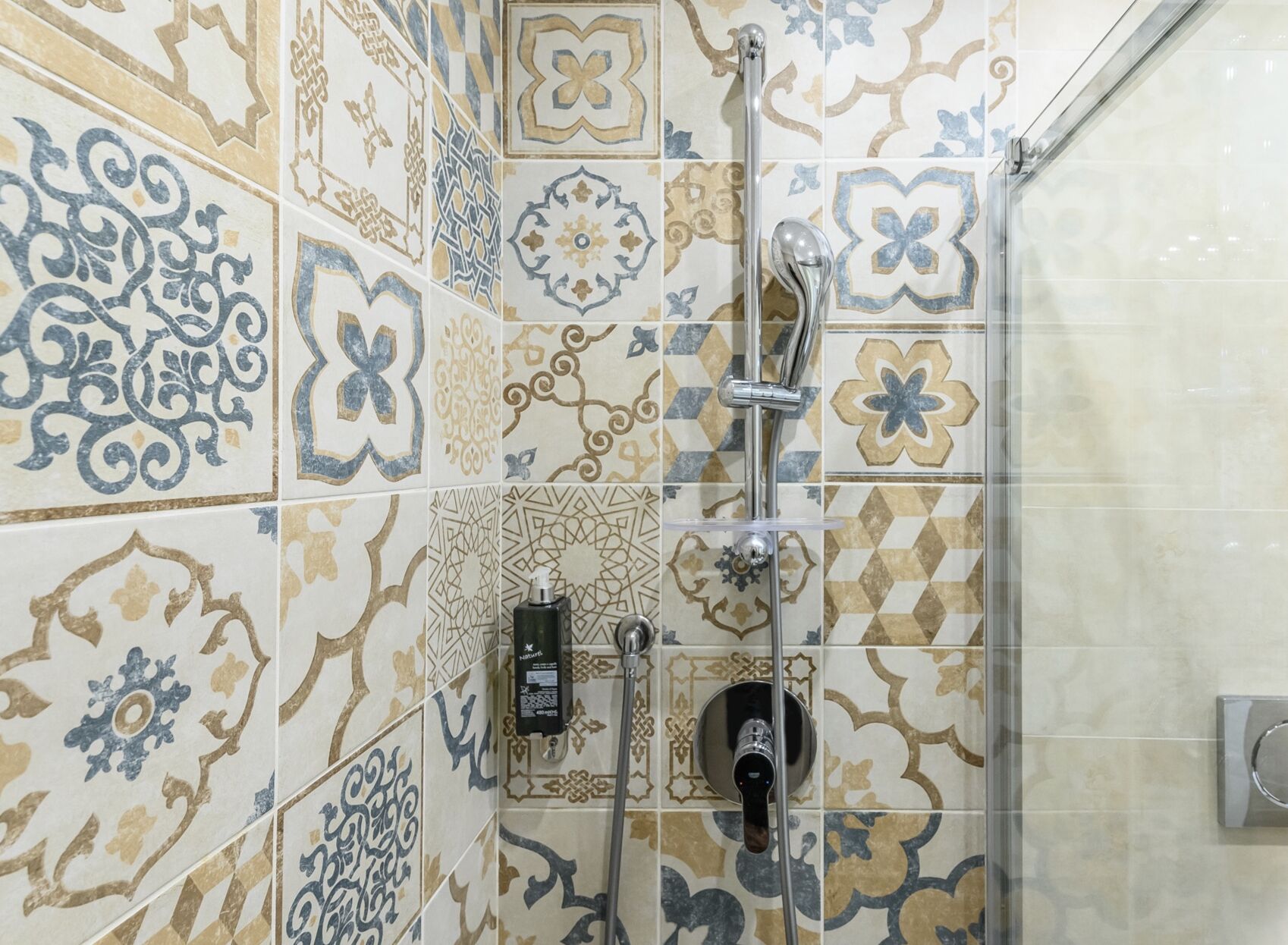 Zona de ducha con azulejos decorativos y cabezal de ducha manual.