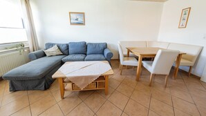 Una sala de estar con un sofá modular, una mesa de comedor con sillas y una ventana con cortinas.