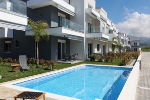 A modern building with a swimming pool, outdoor seating, and a view of the mountains.