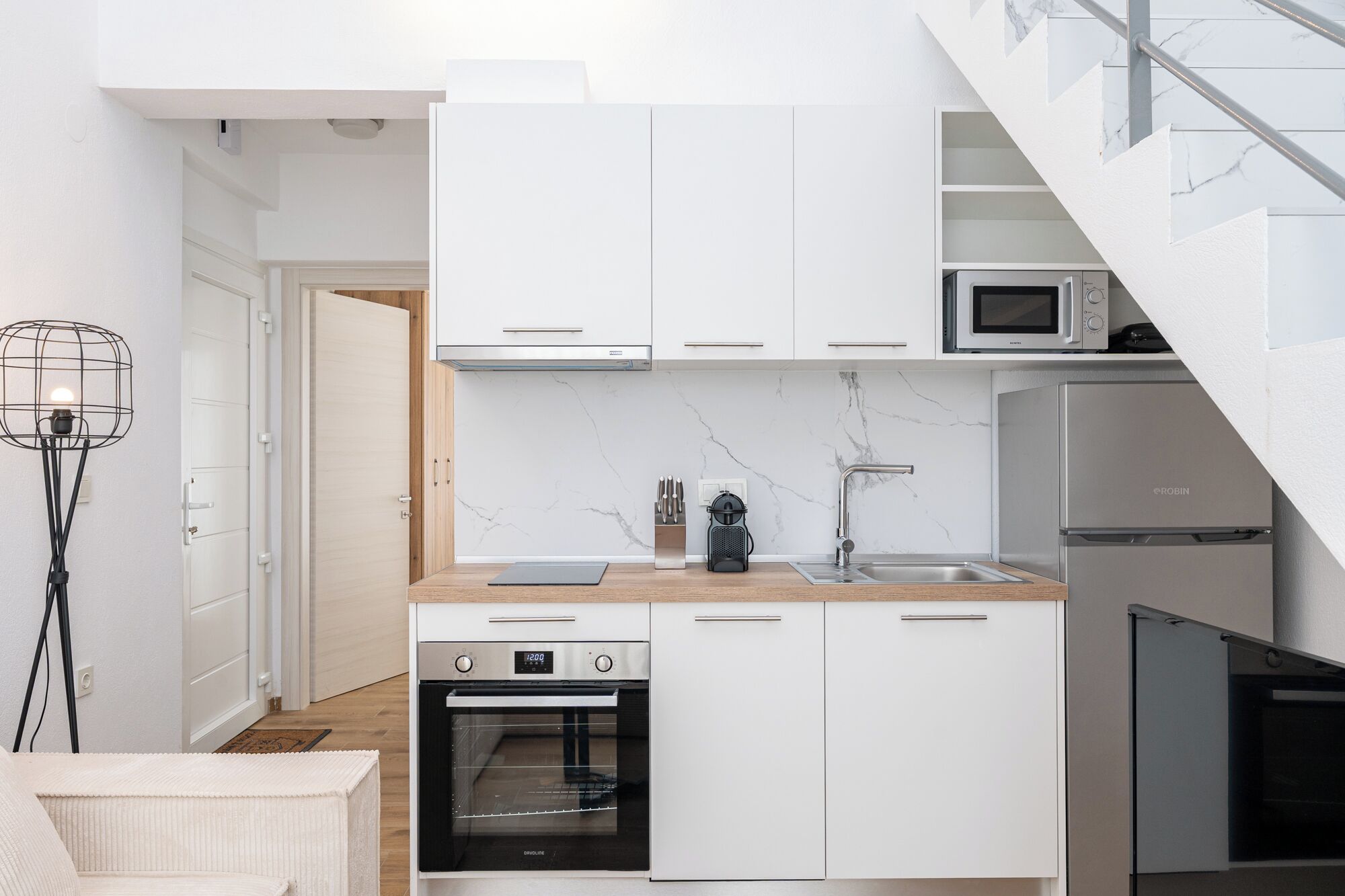 A modern kitchen with white cabinetry, a built-in microwave, a stainless steel refrigerator, and a wooden countertop.
