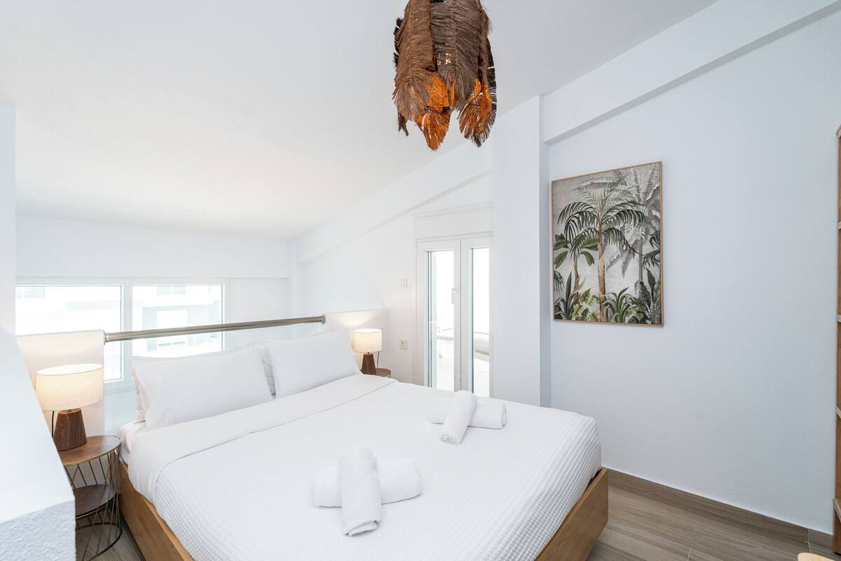 Ein Schlafzimmer mit Bett, weißen Bettwäsche, einer Pendelleuchte, einem Gemälde und einem Fenster.