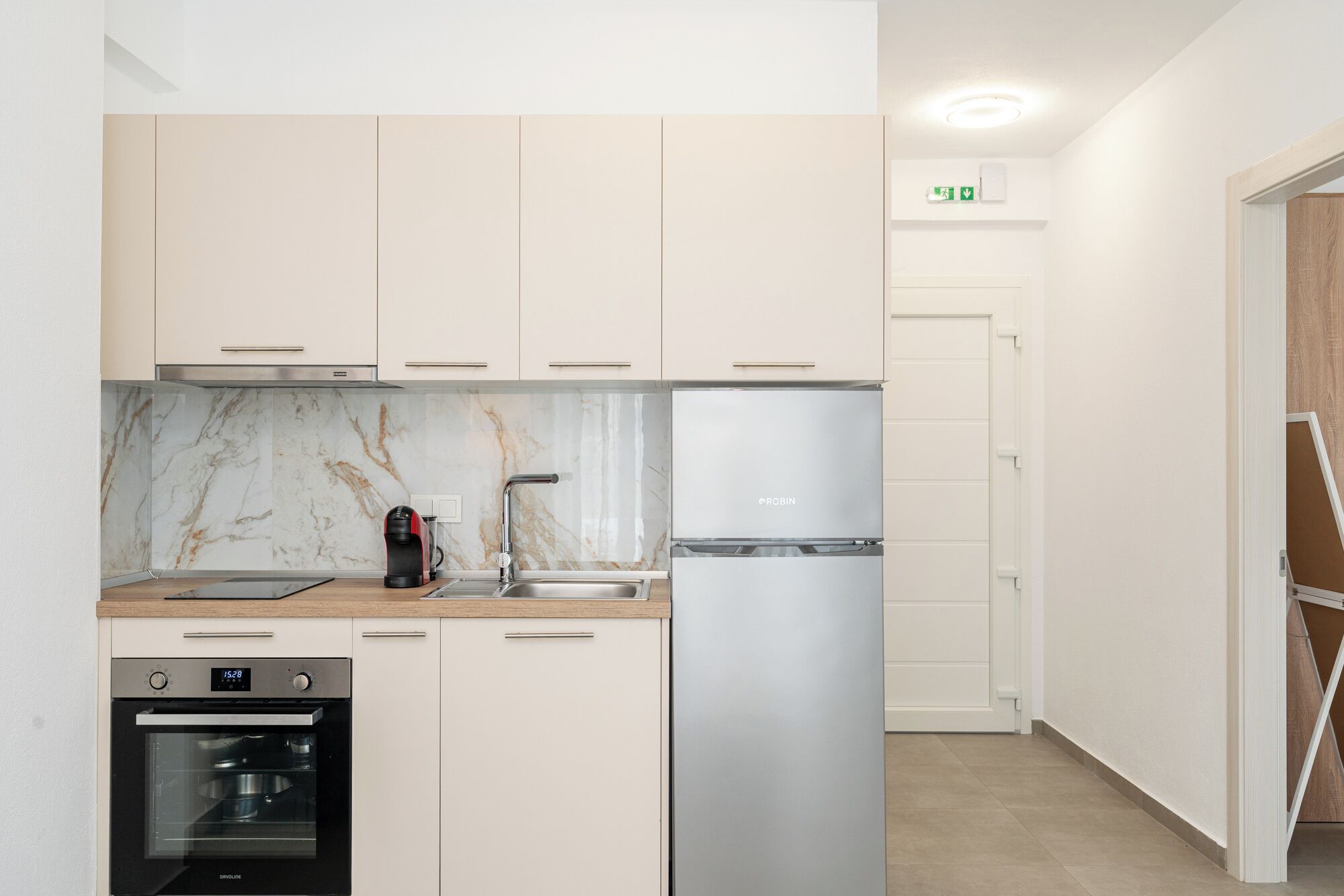 A modern kitchen with a built-in oven, a stainless steel refrigerator, and a marble backsplash.
