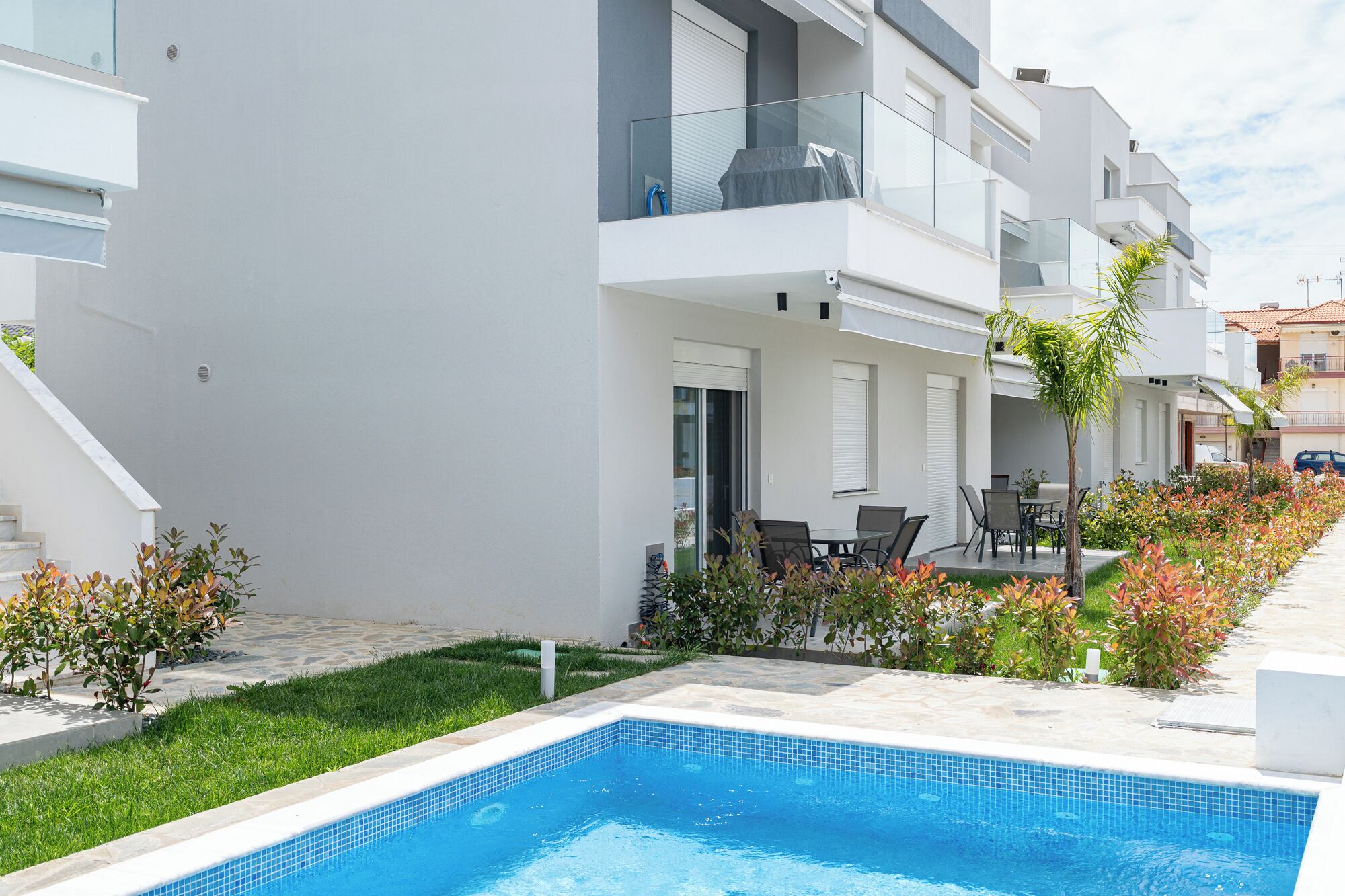 A modern apartment complex with a swimming pool, outdoor seating, and a well-maintained garden.