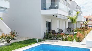 A modern apartment complex with a swimming pool, outdoor seating, and a well-maintained garden.