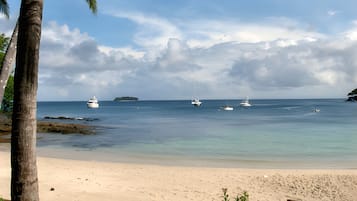 A beach with clear water, boats, and a distant island.