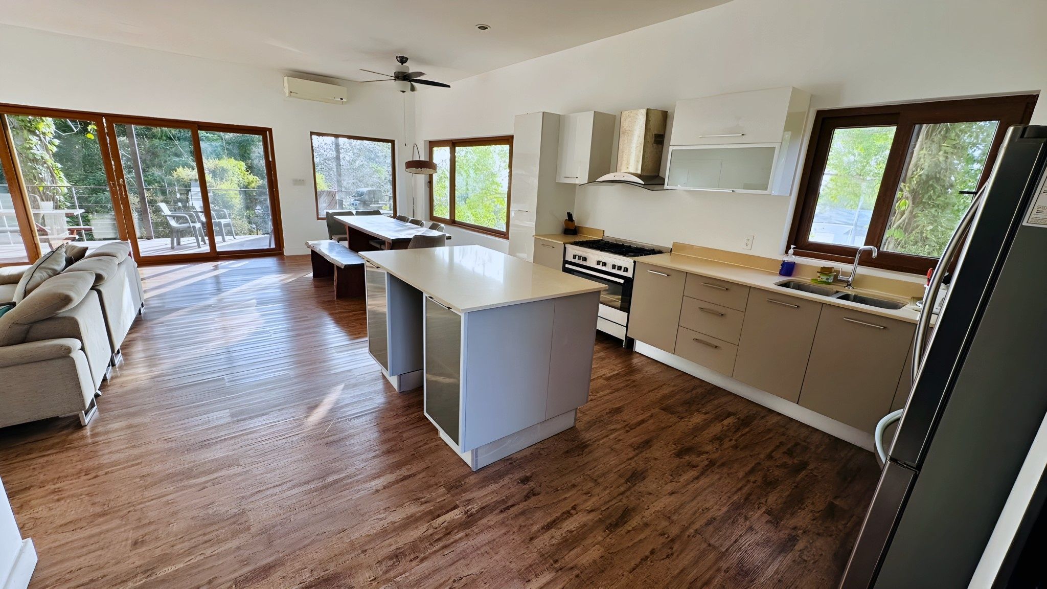 Una cocina moderna con una isla central, piso de madera y grandes ventanales.