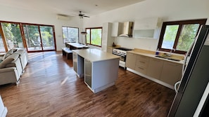 A modern kitchen with a central island, wooden flooring, and large windows. - Gemini Villas Gemini II (Saboga)