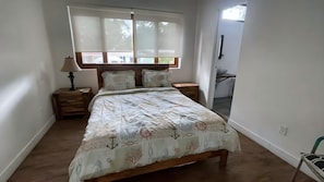 A bedroom with a bed, nightstands, a lamp, a window with blinds, and a view of the outside. - Gemini Villas Gemini II (Saboga)