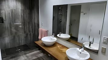 A modern bathroom with two sinks, a wooden vanity, a large mirror, and a shower area.