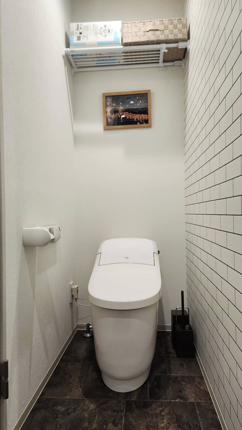 A small, modern bathroom with a white toilet, a wall-mounted air vent, and a framed picture above the toilet.