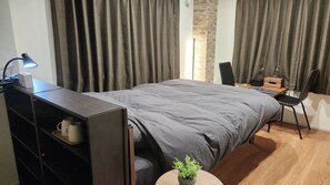 A modern hotel room with a bed, a desk, a chair, a lamp, and a small plant.