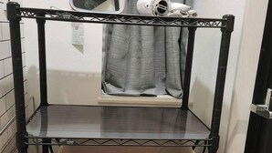 Un baño con un estante metálico negro con cajones etiquetados para ropa, un secador de pelo y un espejo.