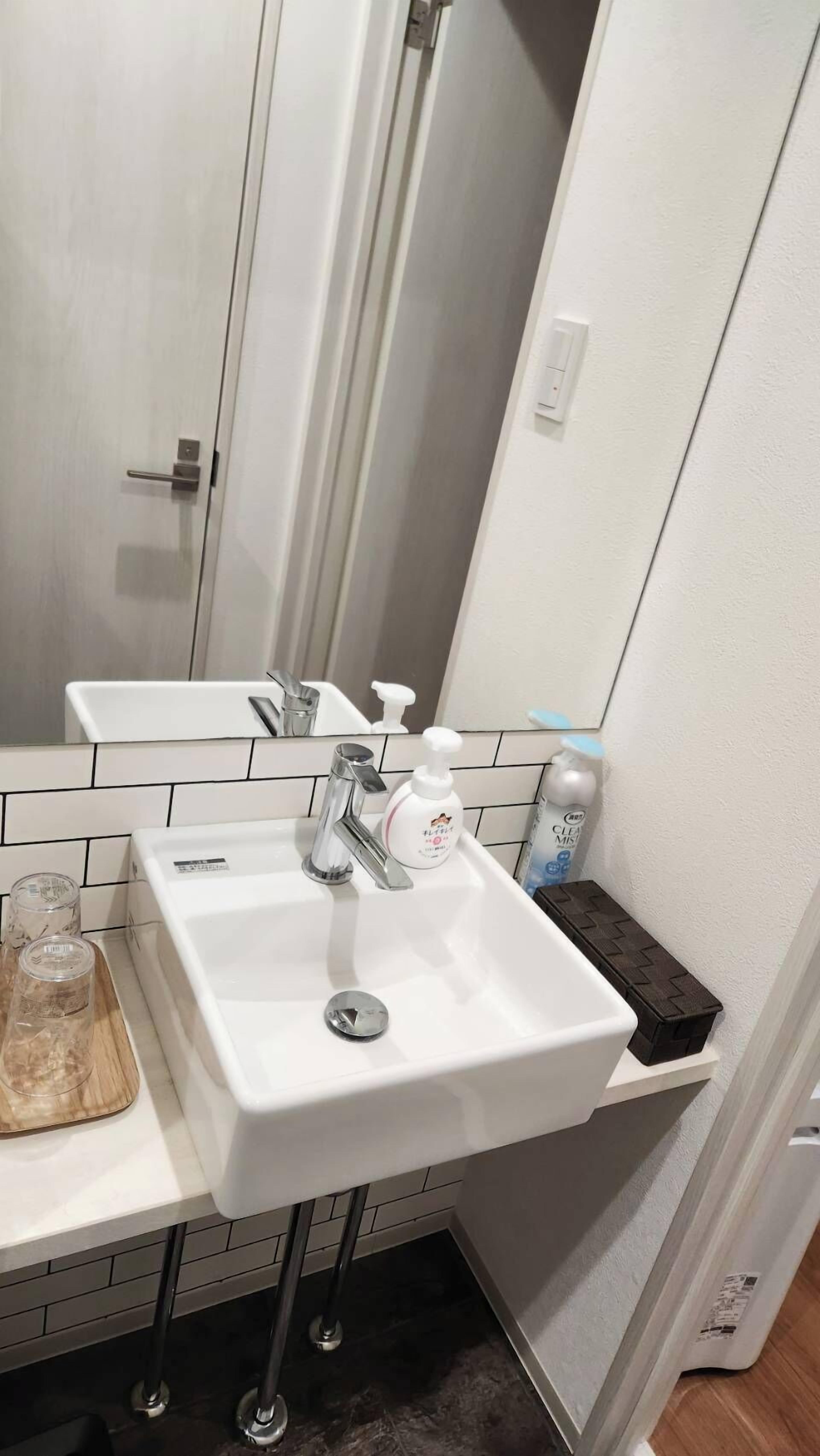 Un baño con lavamanos blanco, un espejo y un estante pequeño con artículos de tocador.