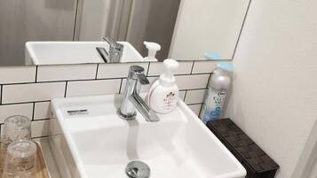 Un baño con lavamanos blanco, un espejo y un estante pequeño con artículos de tocador.