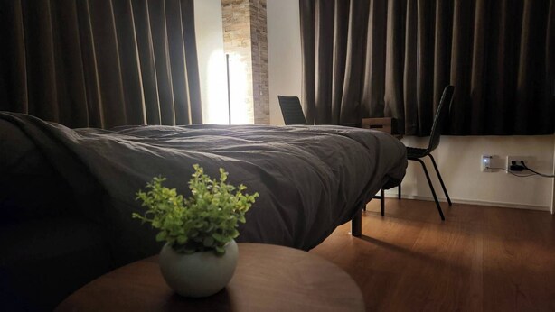 Un dormitorio moderno con una cama grande, una mesita con una planta, una silla y un ventanal con cortinas.