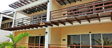 Un edificio de varios pisos con balcones, ventanas amplias y una palmera en primer plano.