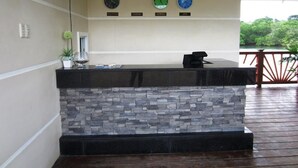 A reception area with a stone counter, clocks displaying different time zones, and a view of greenery outside. - Papakit's Marina and Fishing Lagoon powered by Cocotel (Liloan)