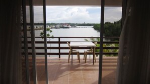 A balcony with a table and chairs, overlooking a body of water with a dock and a house in the distance. - Papakit's Marina and Fishing Lagoon powered by Cocotel (Liloan)
