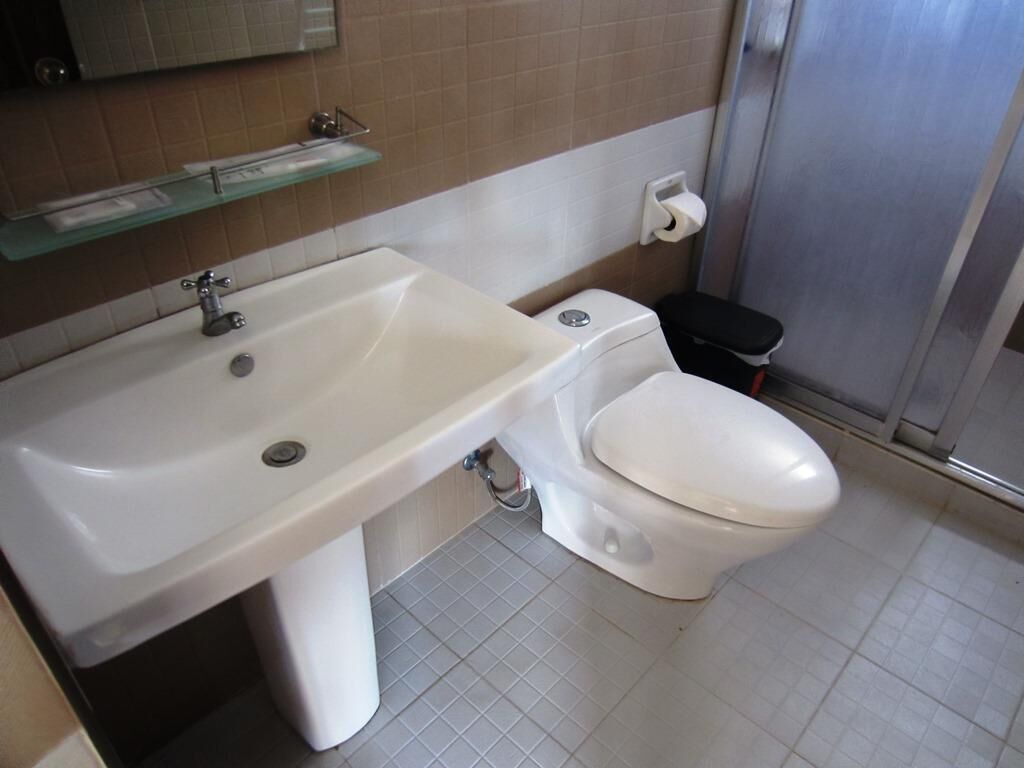 A bathroom with a white sink, toilet, and a glass shelf above the sink.