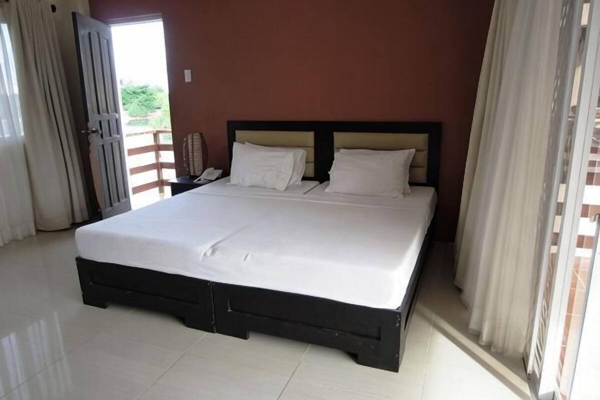 A large bed with a wooden frame, white bedding, and a nightstand with a telephone.