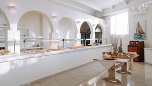 A spacious, modern kitchen with white cabinetry, a long counter with food displays, and a wooden dining table. - Hotiday Room Collection - Naxos (Naxos)
