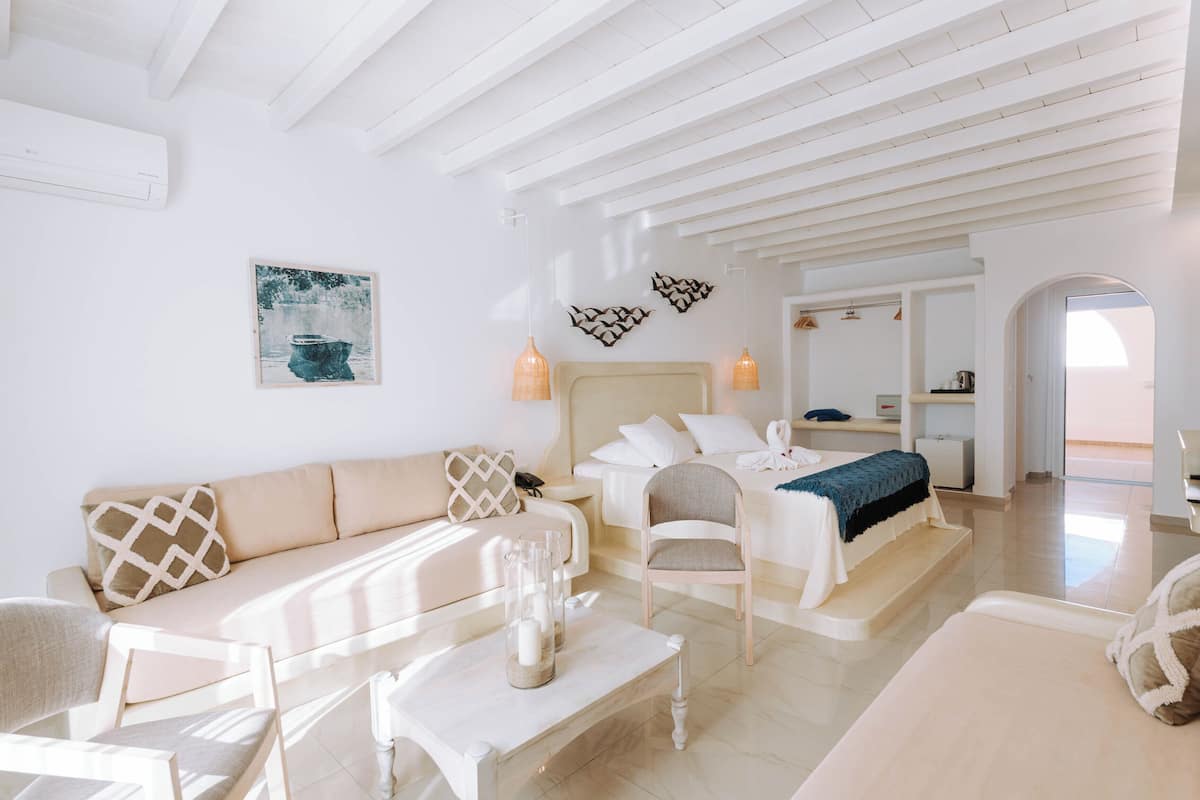Quarto moderno e bem iluminado com sofá, poltrona, cama e uma mesinha com objetos decorativos.
