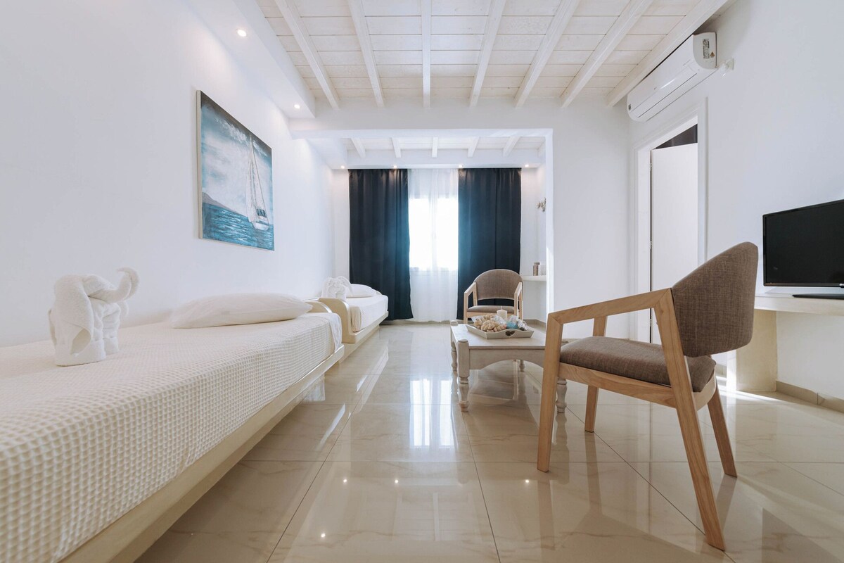 Una habitación de hotel con cama, una silla, un escritorio con computadora y un cuadro en la pared.