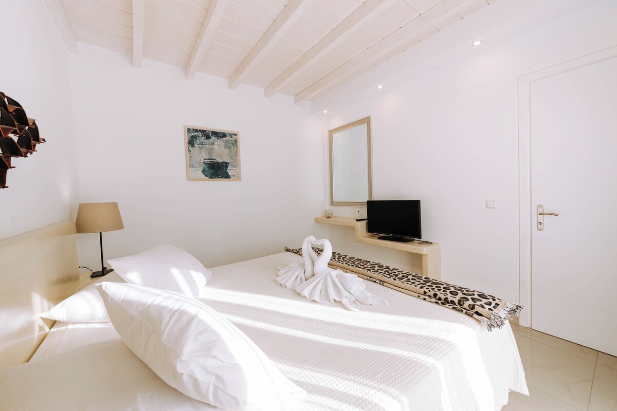 A hotel room with a bed, a television, a mirror, and a painting on the wall.
