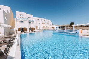 A large swimming pool with lounge chairs and umbrellas, surrounded by white buildings with balconies. - Hotiday Room Collection - Naxos (Naxos)