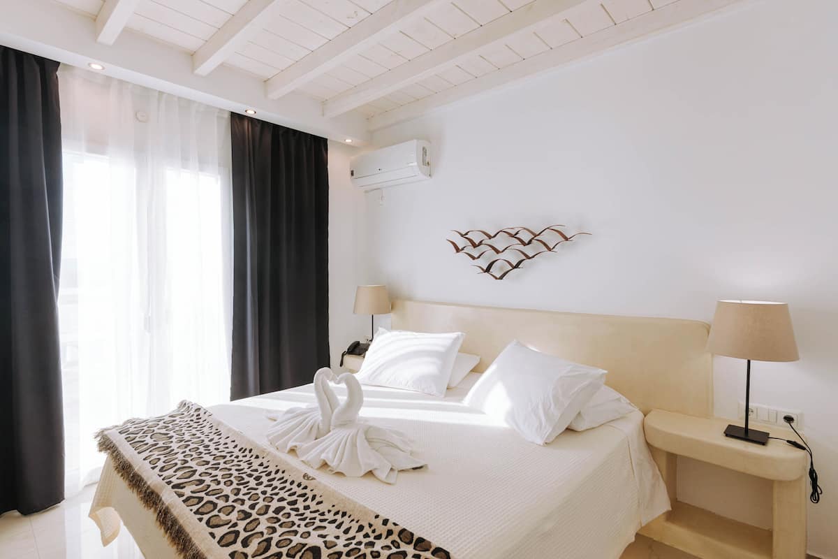 Quarto de hotel com uma cama, duas mesas de cabeceira, ar condicionado fixado na parede e um objeto decorativo na parede.