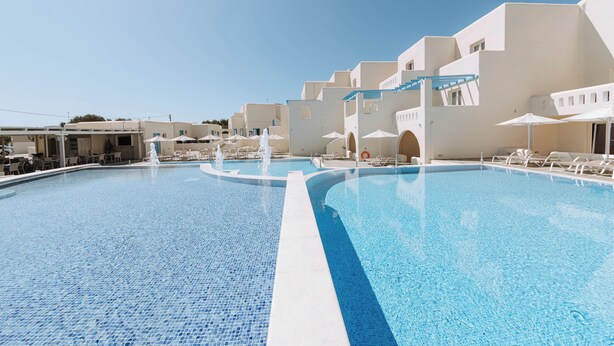 A large, clear swimming pool with white lounge chairs and umbrellas, surrounded by white buildings with balconies. - Hotiday Room Collection - Naxos (Naxos)