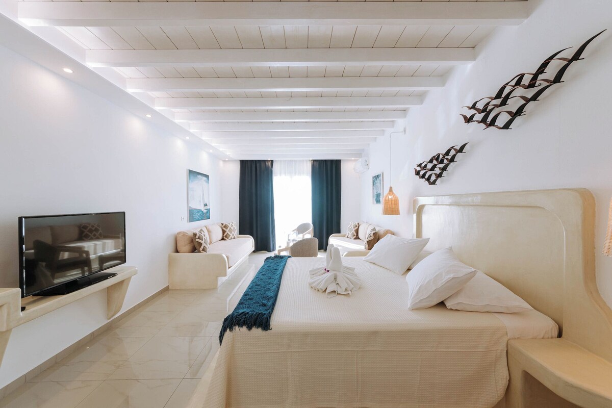 Une chambre d’hôtel avec un lit, une télévision, un canapé, un fauteuil et une grande fenêtre.