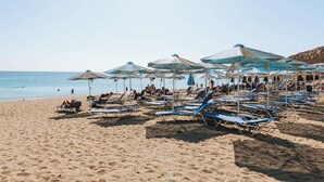 A beach with rows of sun loungers and umbrellas, people relaxing, and the ocean in the background. - Hotiday Room Collection - Naxos (Naxos)