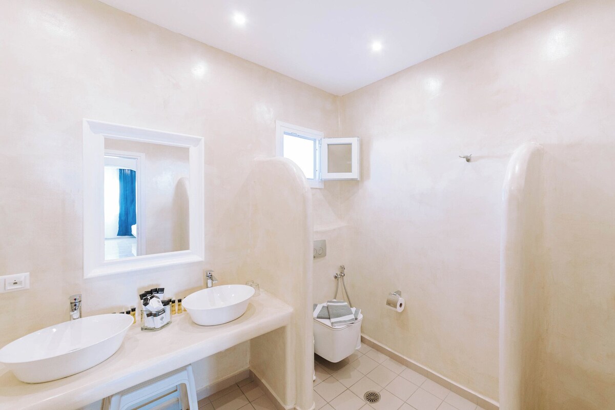 A bathroom with two sinks, a mirror, a shower, and a toilet.