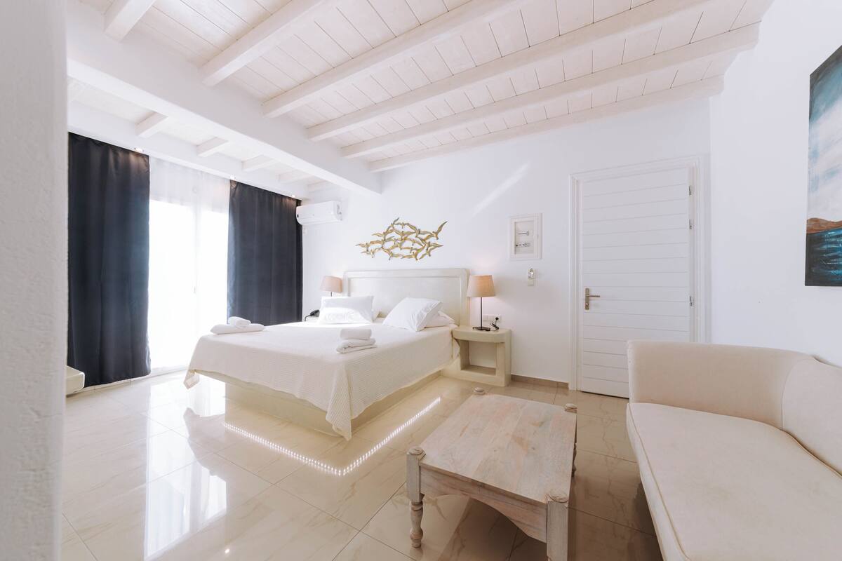 Quarto de hotel com uma cama grande, mesas de cabeceira, um sofá e um quadro na parede.