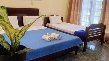 Habitación de hotel con dos camas individuales, una colcha azul, almohadas blancas, una silla de madera, una planta en maceta y un cuadro en la pared.