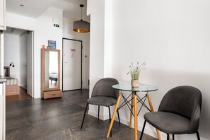 A modern hotel lobby with a glass table, two grey chairs, a wooden cabinet, and a mirror. - Glimmer 2-Bedroom Apartment in Athens (Athens)