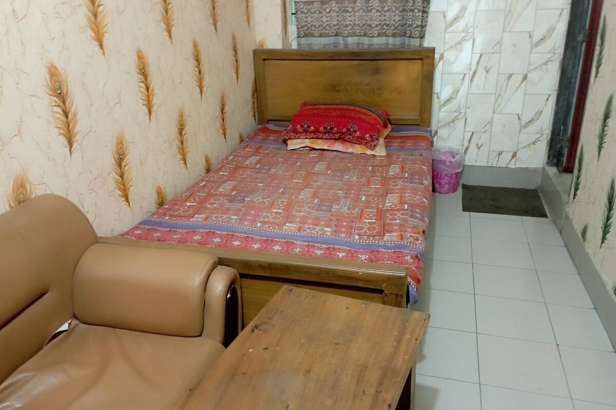 A small, neatly arranged room with a single bed, a wooden nightstand, and a brown leather chair.
