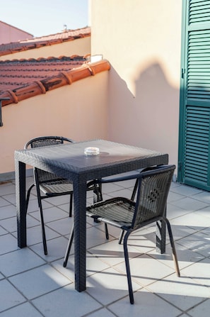 A small outdoor patio with a square table and two chairs, a tiled floor, and a green door in the background. - Hotel 3 Comfort and Serenity Heart of Ventimiglia (Ventimiglia)