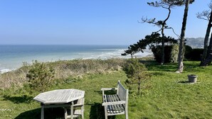A wooden bench and table set on a grassy area overlooking a beach with clear skies. - Le Nid des Falaises, au bord de la plage (Varengeville-sur-Mer)