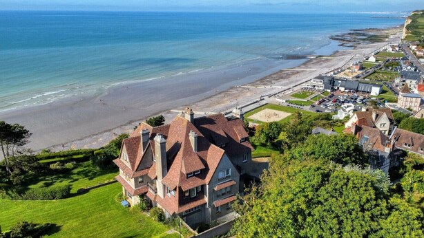A large, historic house with multiple chimneys, situated on a lush green lawn with a view of the ocean and beach. - Le Nid des Falaises, au bord de la plage (Varengeville-sur-Mer)