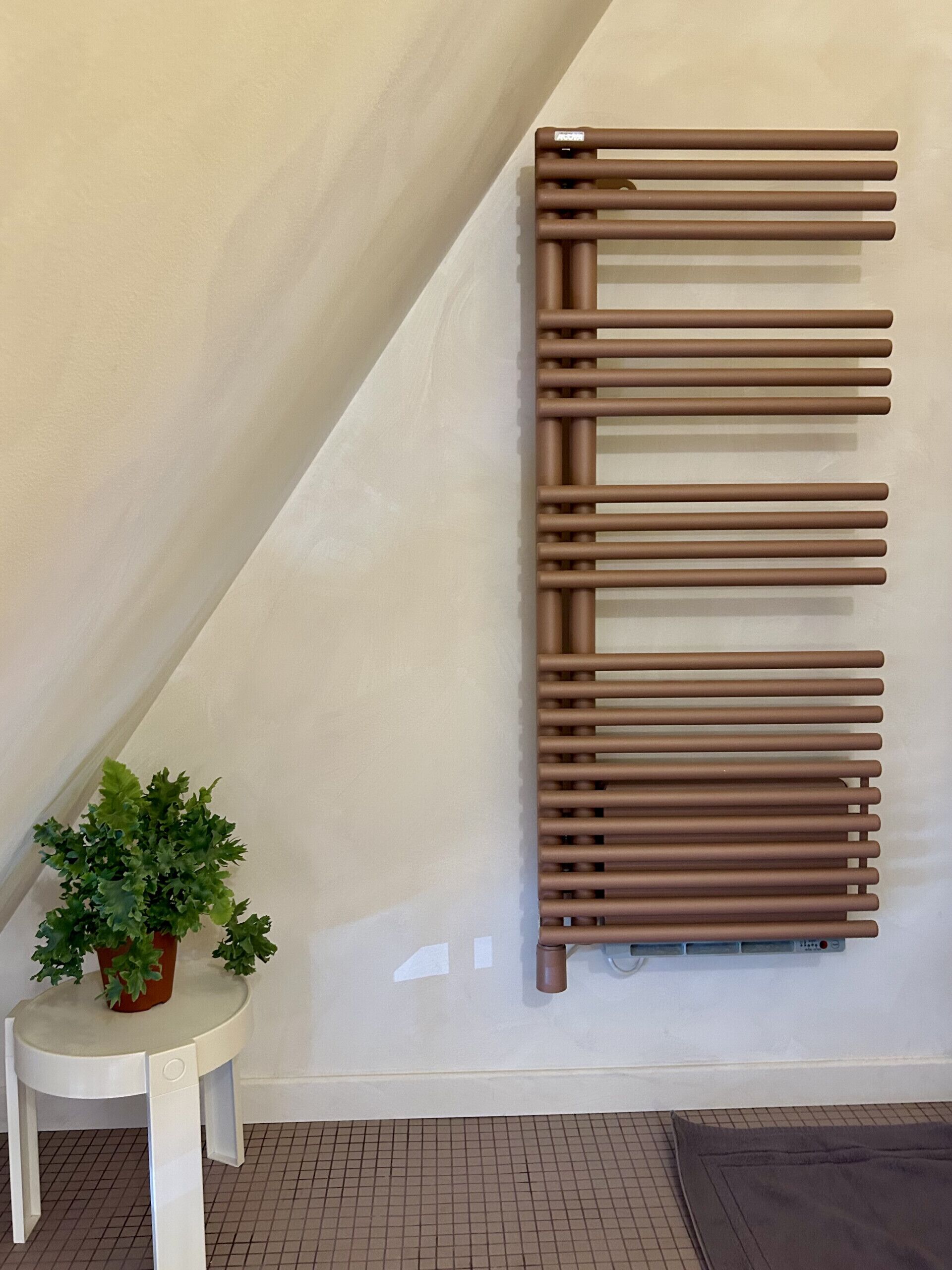 Une pièce moderne avec un mur blanc, un radiateur, une petite table blanche ornée d’une plante en pot et un sol carrelé.