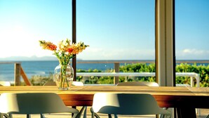 A table with a vase of flowers and a view of the ocean. - Nine Mile Beach House - Holiday Houses Tasmania (Glamorgan-Spring Bay)