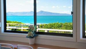 A room with a large window overlooking a coastal view with greenery and mountains. - Nine Mile Beach House - Holiday Houses Tasmania (Glamorgan-Spring Bay)