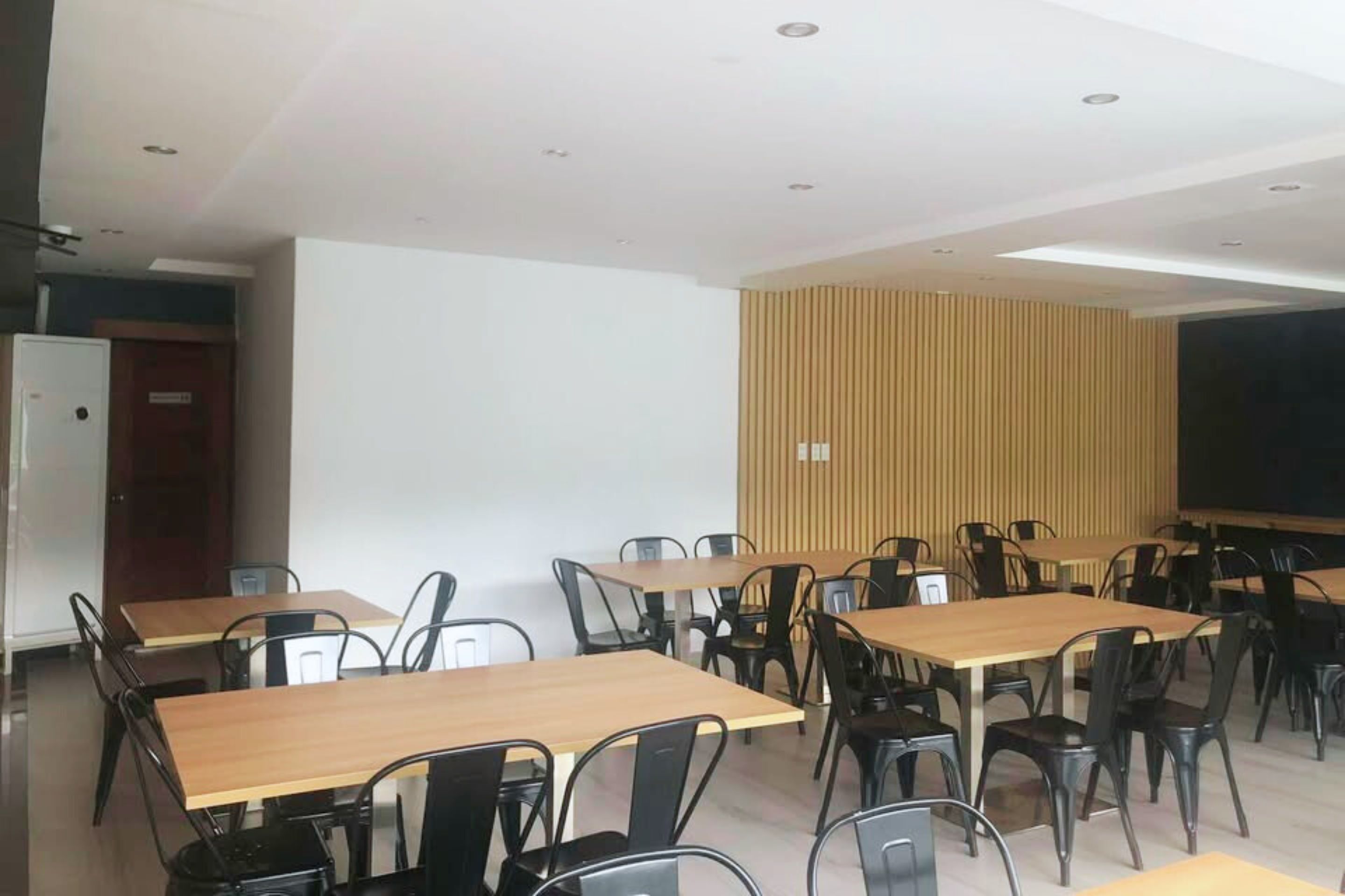 A conference room with multiple tables and chairs, white walls, and a wooden panel wall.